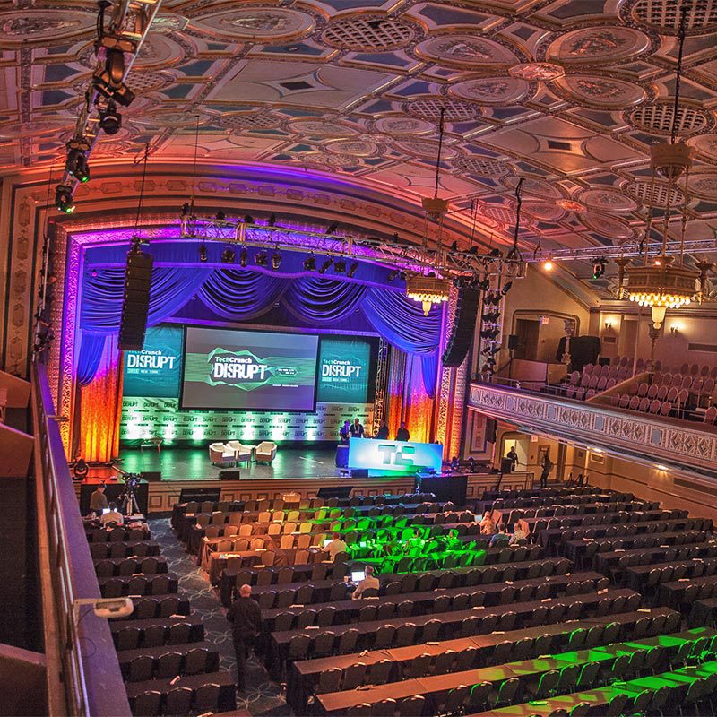 grand-events2 A spacious auditorium featuring a stage and a large screen, designed for presentations and performances.